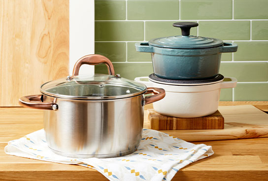 Assortment of stainless steel & ceramic cookware, with a kitchen towel & cutting boards.