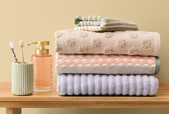 A stack of plush, patterned towels and washcloths next to a colorful soap dispenser & stylish toothbrush holder.